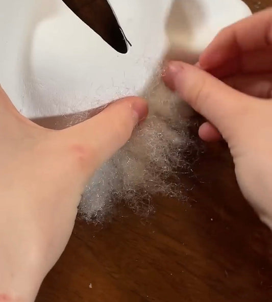 an action shot of someone gluing polyfill stuffing onto a therian paper cat mask on a brown dining table